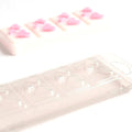 Klar plastbeholder for vokssmelt med hjerteformer, og en ferdig hvit vokssmelt med rosa hjerter i bakgrunnen