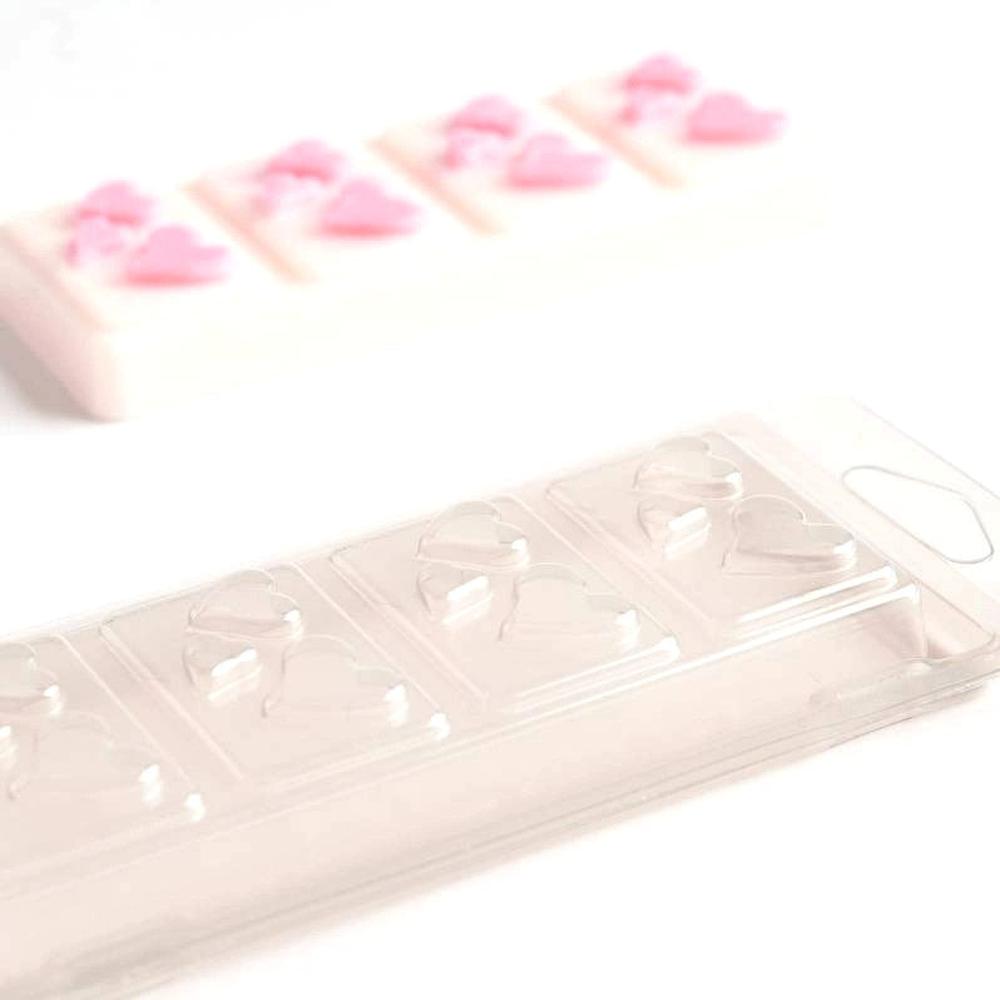 Klar plastbeholder for vokssmelt med hjerteformer, og en ferdig hvit vokssmelt med rosa hjerter i bakgrunnen