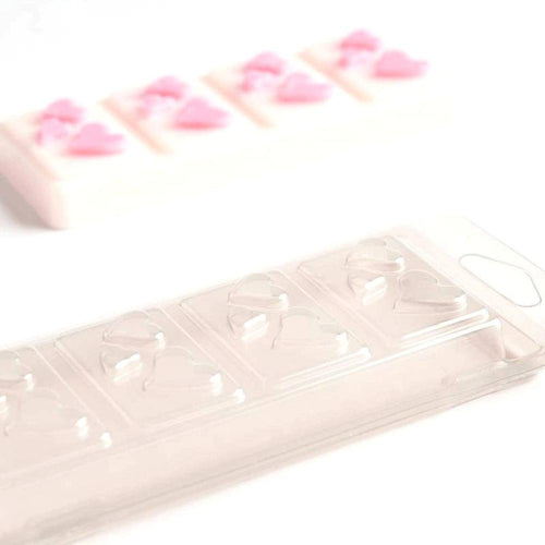 Klar plastbeholder for vokssmelt med hjerteformer, og en ferdig hvit vokssmelt med rosa hjerter i bakgrunnen