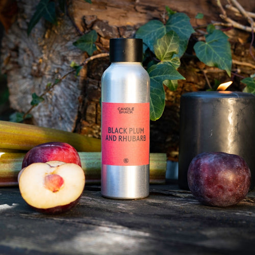 Sølvfarget flaske med Black Plum and Rhubarb duftolje, svarte plommer, rabarbra og et tent svart lys