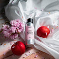 Sølvfarget flaske med "Cherry Blossom and Plum" duftolje, rosa kirsebærblomster og røde plommer på hvit silke.