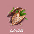 Kakao- og patchouli-duftolje med åpne og hele kakaobønner og grønne blader på rosa bakgrunn