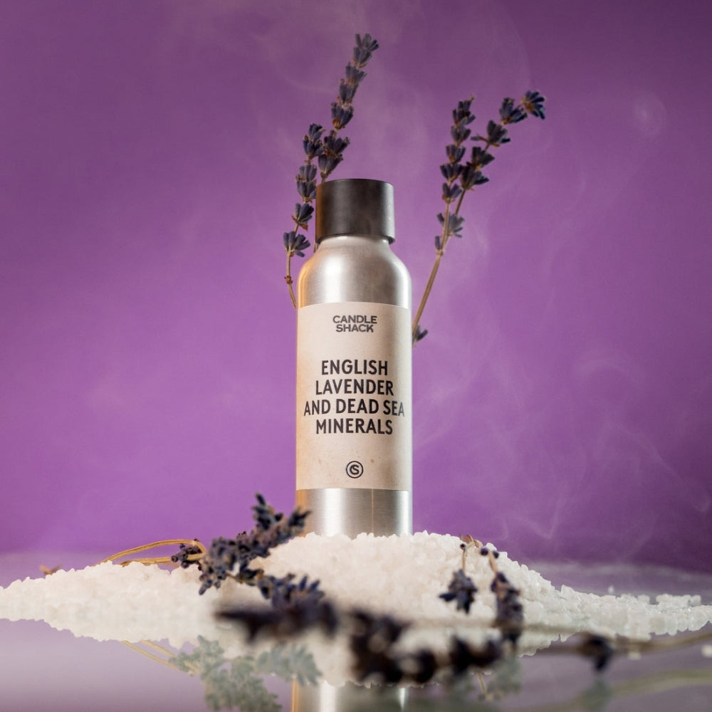 Sølvfarget flaske med "English Lavender and Dead Sea Minerals" etikett, omgitt av lavendel og hvitt salt på lilla bakgrunn