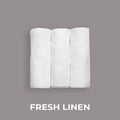 Tre hvite, sammenrullede håndklær på grå bakgrunn, merket "Fresh Linen