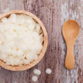 Hvit bivoks i pastiller i en trebol, med en treskje og noen løse pastiller på et treunderlag