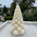 Hvitt juletrelys med kuler, 14 cm høyt, på marmorbrett, mot grønne trær