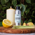 Sølvfarget flaske med Lemongrass and Ginger duftolje, sitron, ingefær, sitrongress og et brennende lys på trefjøl