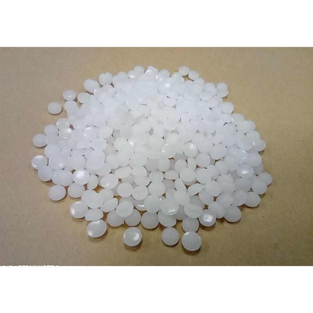 Hvit parafinvoks i små, runde pellets på en brun overflate.