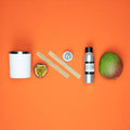 Startpakke for lysstøping med hvit beholder, treveker, pasjonsfrukt, mango og duftolje på oransje bakgrunn