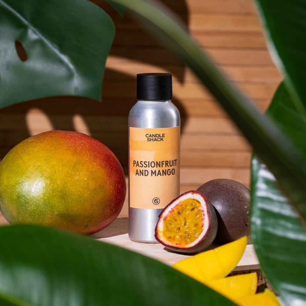 Sølvfarget flaske med Passionfruit and Mango duftolje, hel mango, og delt pasjonsfrukt og mangoskiver