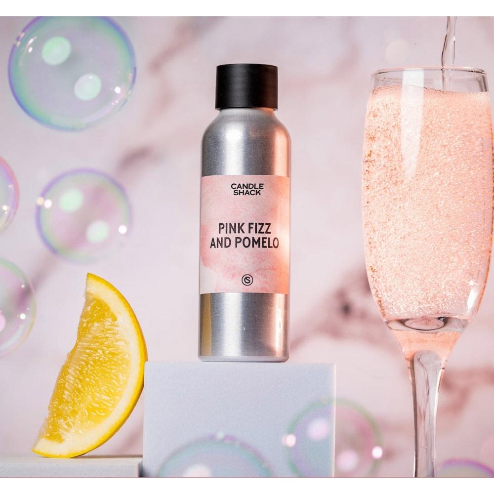 Sølvfarget flaske med Pink Fizz & Pomelo duftolje, et glass rosa musserende drikke og en sitronskive.
