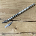 Sølv presisjonskniv/hobbykniv med metallhåndtak og utskiftbart blad, pluss et løst ekstra blad, på trebakgrunn