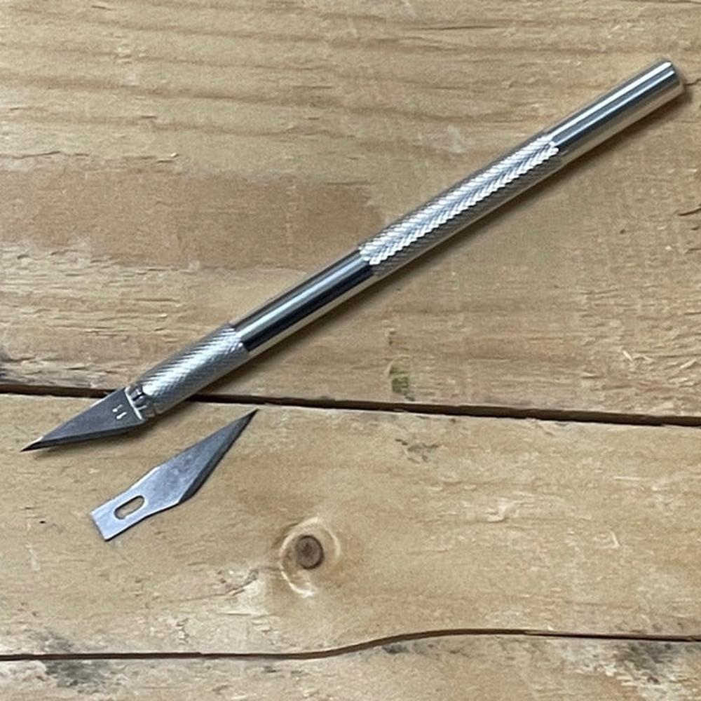 Sølv presisjonskniv/hobbykniv med metallhåndtak og utskiftbart blad, pluss et løst ekstra blad, på trebakgrunn