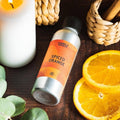 Sølvfarget flaske med Spiced Orange duftolje, brennende hvitt lys, appelsinskiver og kurv på treoverflate